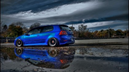 Volkswagen Golf di color Blue con riflesso su asfalto bagnato